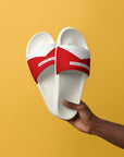 The Red's pool slides, red and white strap on white sole, held against yellow